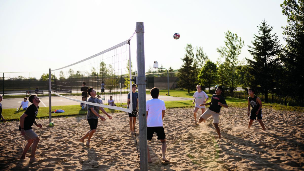 Eine Gruppe junger Leute spielt Beach Volleyball an einem Sommerabend.