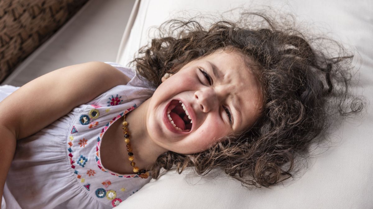 Ein etwa 4 jähriges Mädchen liegt in einem Bett und ist sichtlich wütend, denn ihre Stirn ist gerunzelt und der Mund zu einem Schrei geöffnet.