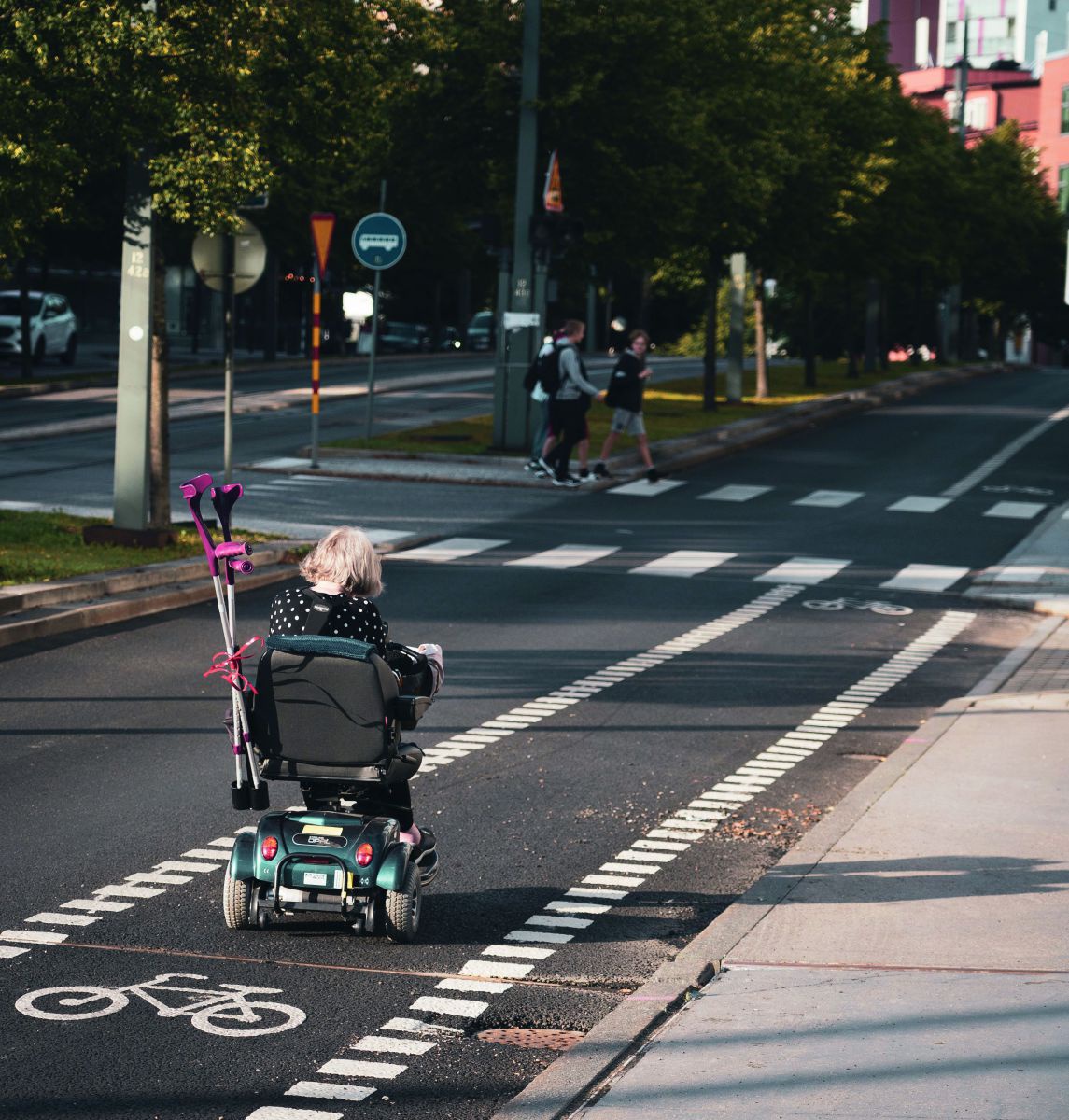 Eine alte Person fährt mit dem Elektroroller auf dem Radweg.