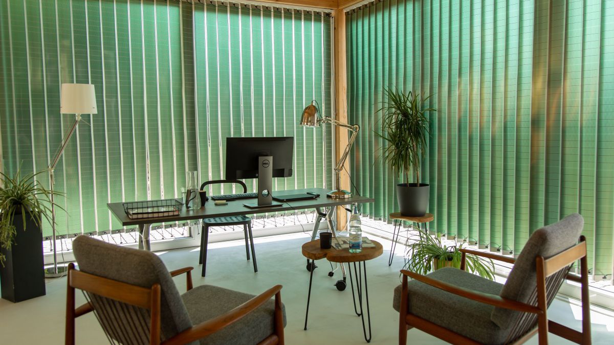 Ein Büroraum mit raumhohen Fenstern wird von Lamellenvorhängen aus flexiblen Photovoltaikelementen angenehm abgedunkelt.