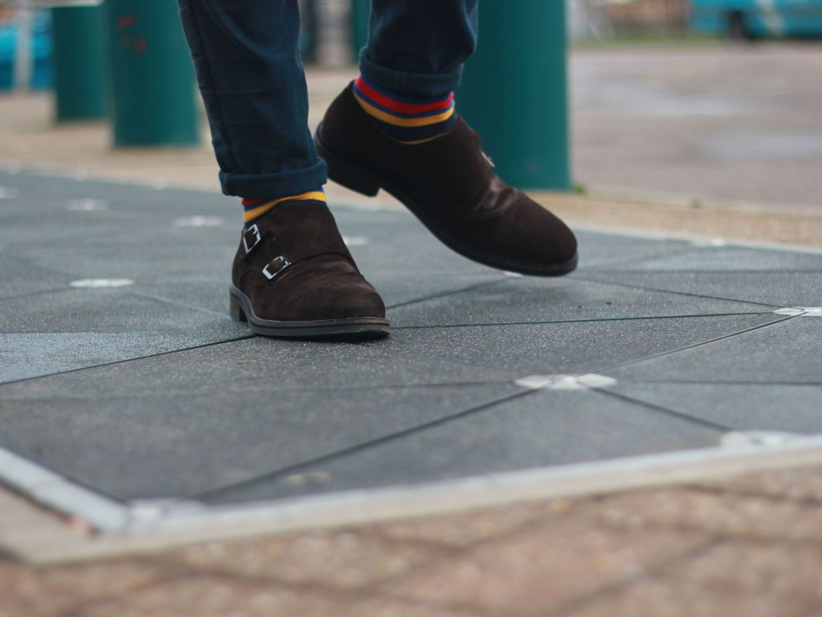 Eine Person, von der man nur die beschuhten Füße sieht, tritt über spezielle Platten im Boden eines öffentlichen Platzes.