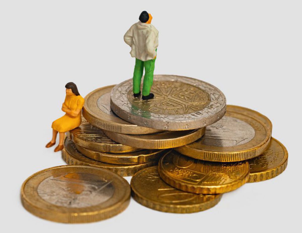 Ein kleiner Berg aus Euro- und Cent-Münzen, auf dem Gipfel steht eine Modellfigur uns sieht in die unbestimmte Ferne, weiter unten sitzt eine weitere Figur mit dem Rücken zur anderen mit verschränkten Armen.