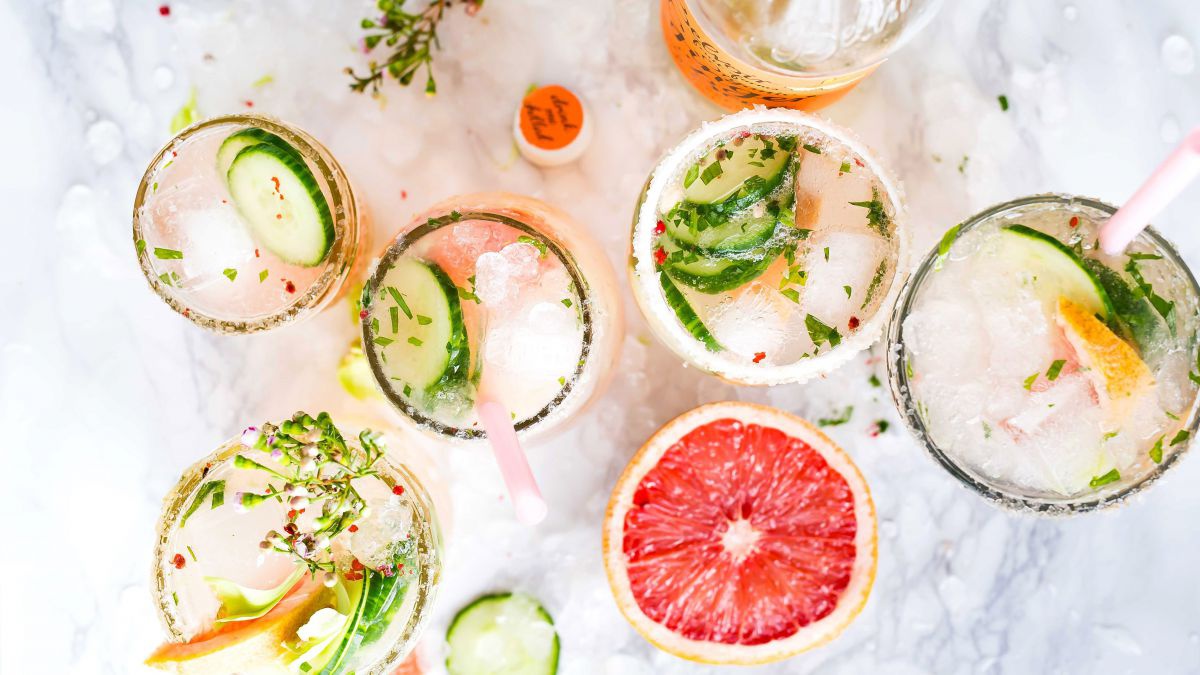 Mehrere Cocktailgläser mit Kräutern, Blutorangen und Gurken dekoriert von oben fotografiert.