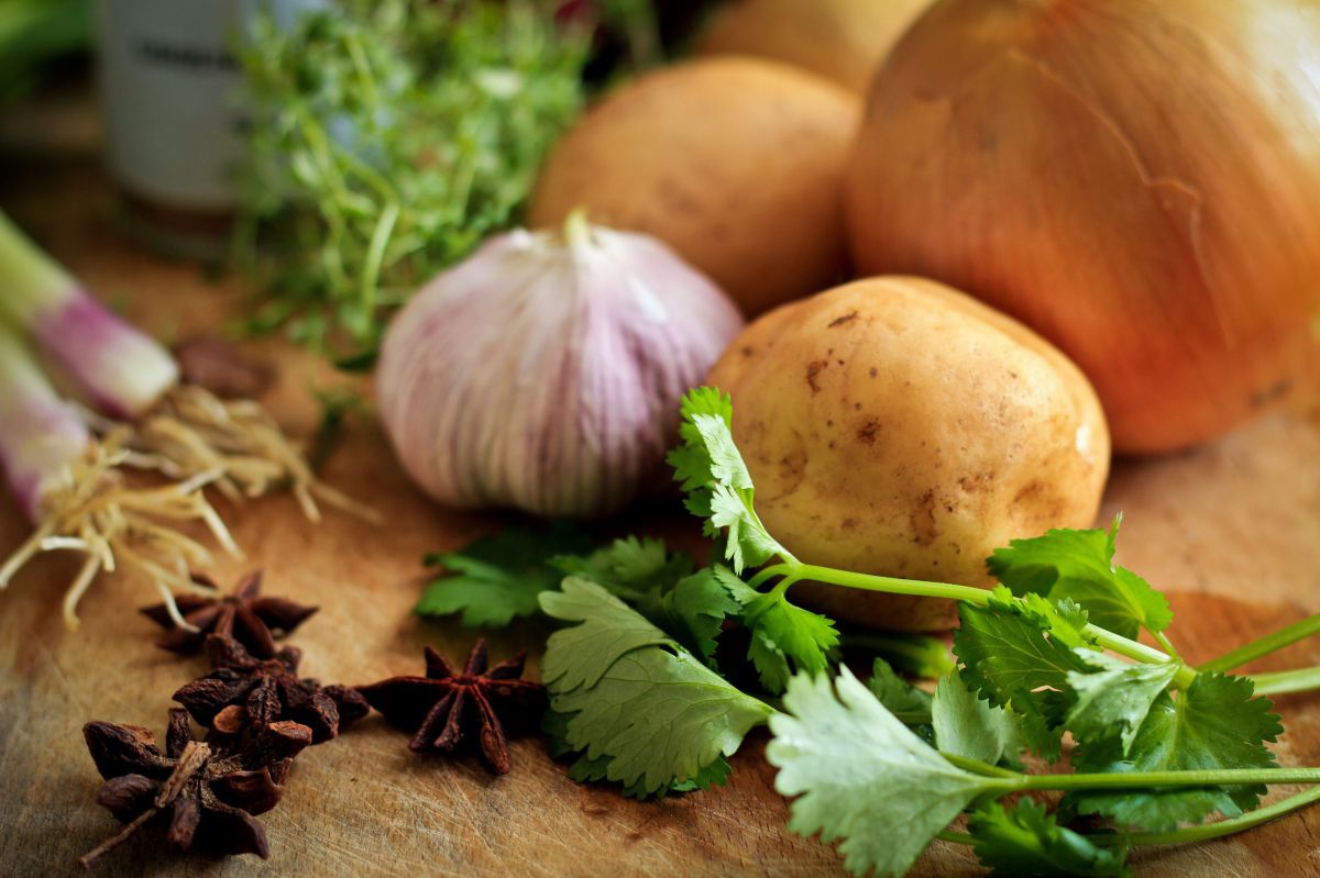 Auf einem Brett liegen Kartoffeln, Knoblauch, Sternanis, Petersilie und Frühlingszwiebel.
