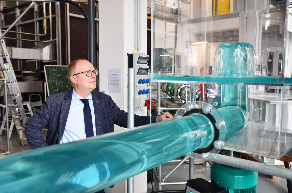 Ein Mann mit Brille und kurzen Haaren steht in einem Labor hinter einem Rohr, durch das Wasser fließt.