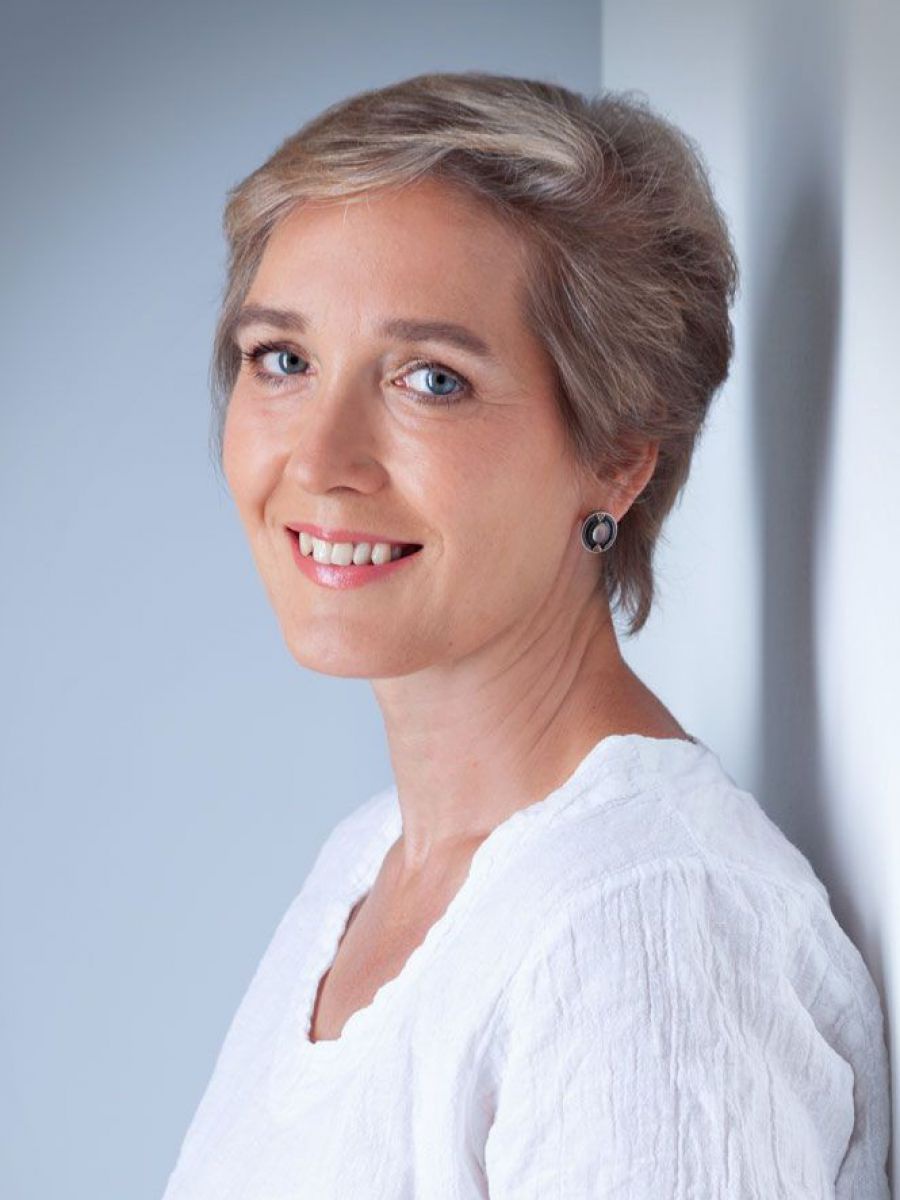 Eine Frau mit kurzen hellen Haaren und blauen Augen blickt lächelnd in die Kamera.