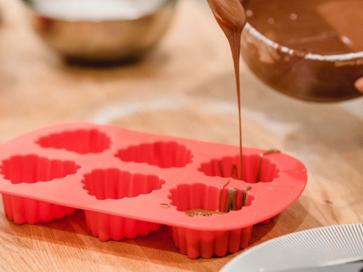 Mit einem Löffel wird Schokoladencreme in eine Silikonbackform gefüllt.