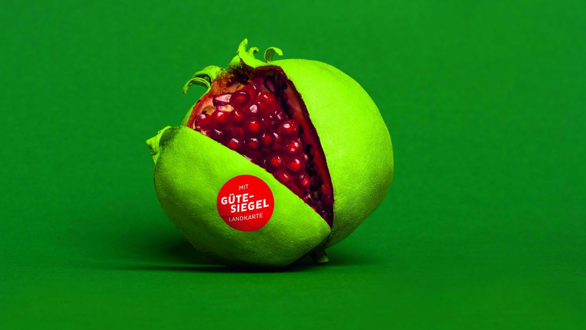 Ein außen grün angesprühter Granatapfel halb aufgeschnitten vor grünem Hintergrund.