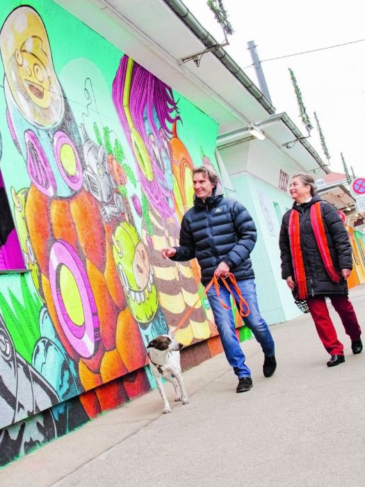 Ein Fußgängerpaar mit Hund passiert das farbenfrohe Mural am Schlingermarkt.
