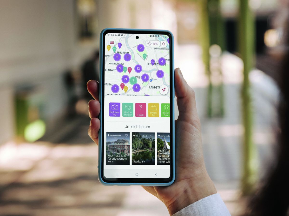 Eine weibliche Hand hält ihr Smartphone ins Bild. Wir sehen auf dem Bildschirm eine App geöffnet, über die geführte Stadtspaziergänge in Wien angeboten werden. 