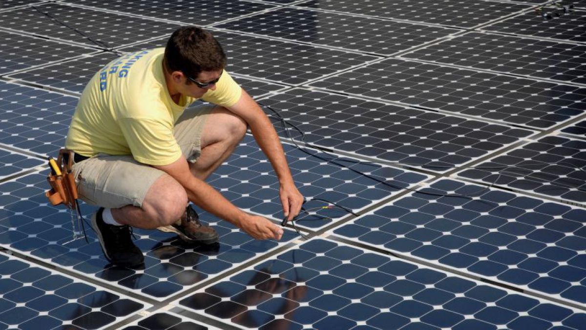 Ein Mann kniet bei der Montage auf Solarpanelen.