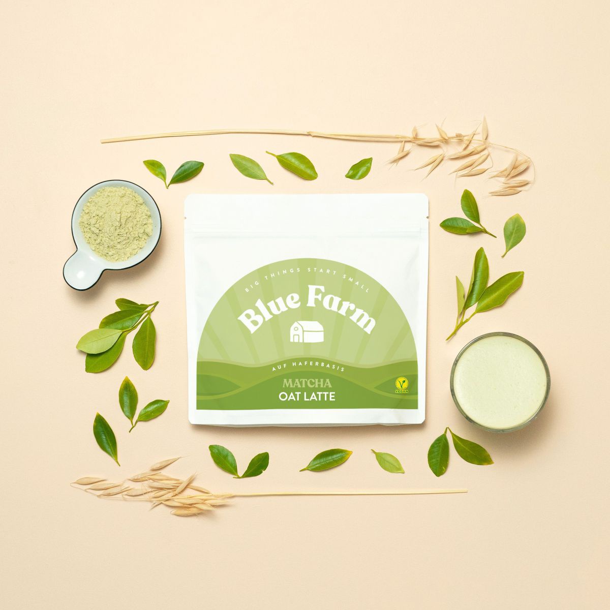 In der Mitte liegt ein Beutel Matcha Oat Latte, rundherum sind Hafer, Blätter, Matchapulver und ein gefülltes Glas angeordnet.