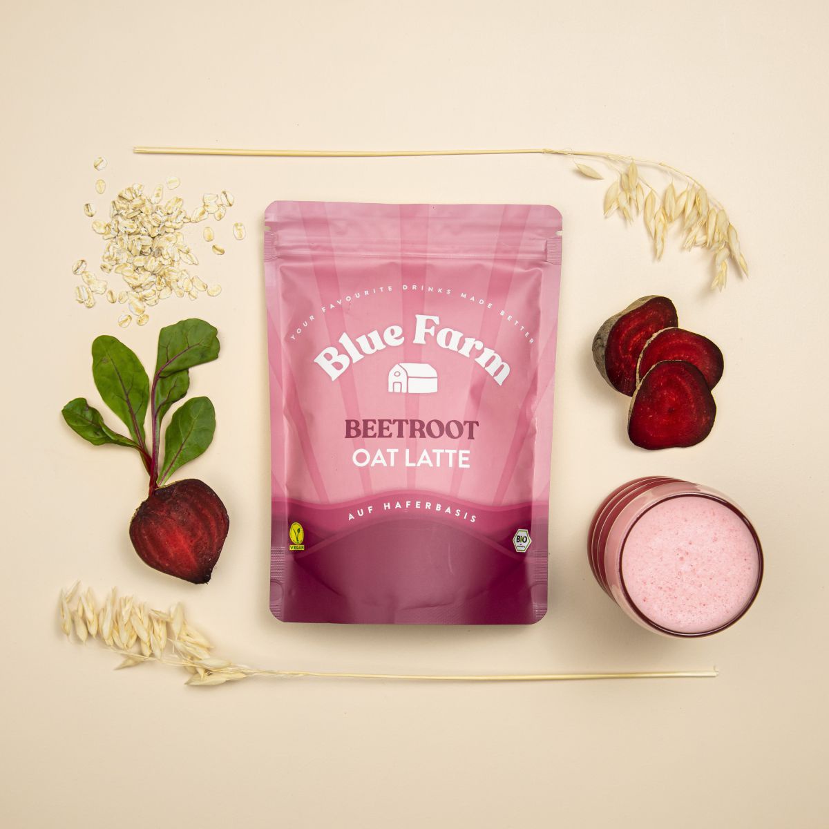In der Mitte liegt ein Beutel Beetroot Oat Latte, rundherum sind Hafer, rote Rüben und ein gefülltes Glas angeordnet. 