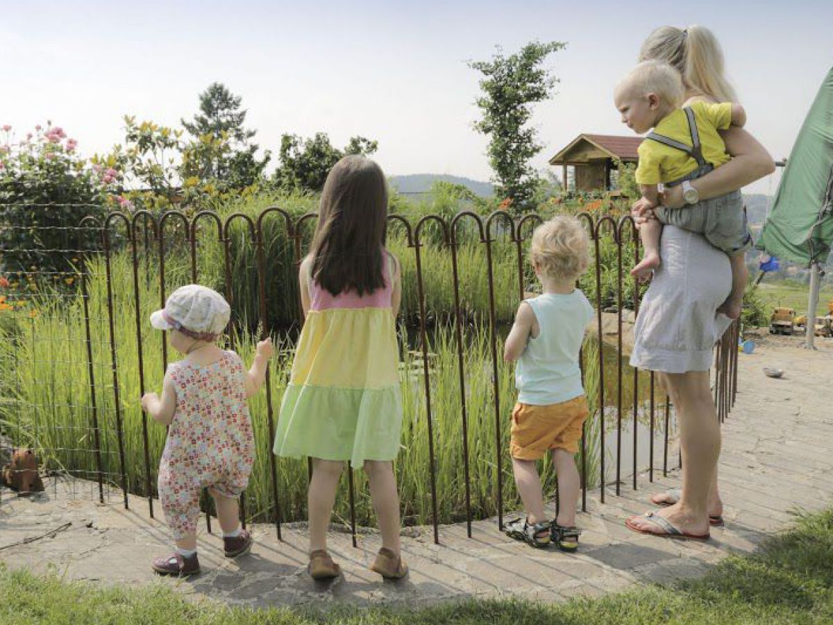 Eine Frau mit einem Kleinkind auf der Hüfte und drei weitere Kinder stehen vor einem durch eine Absperrung gesicherten Gartenteich.