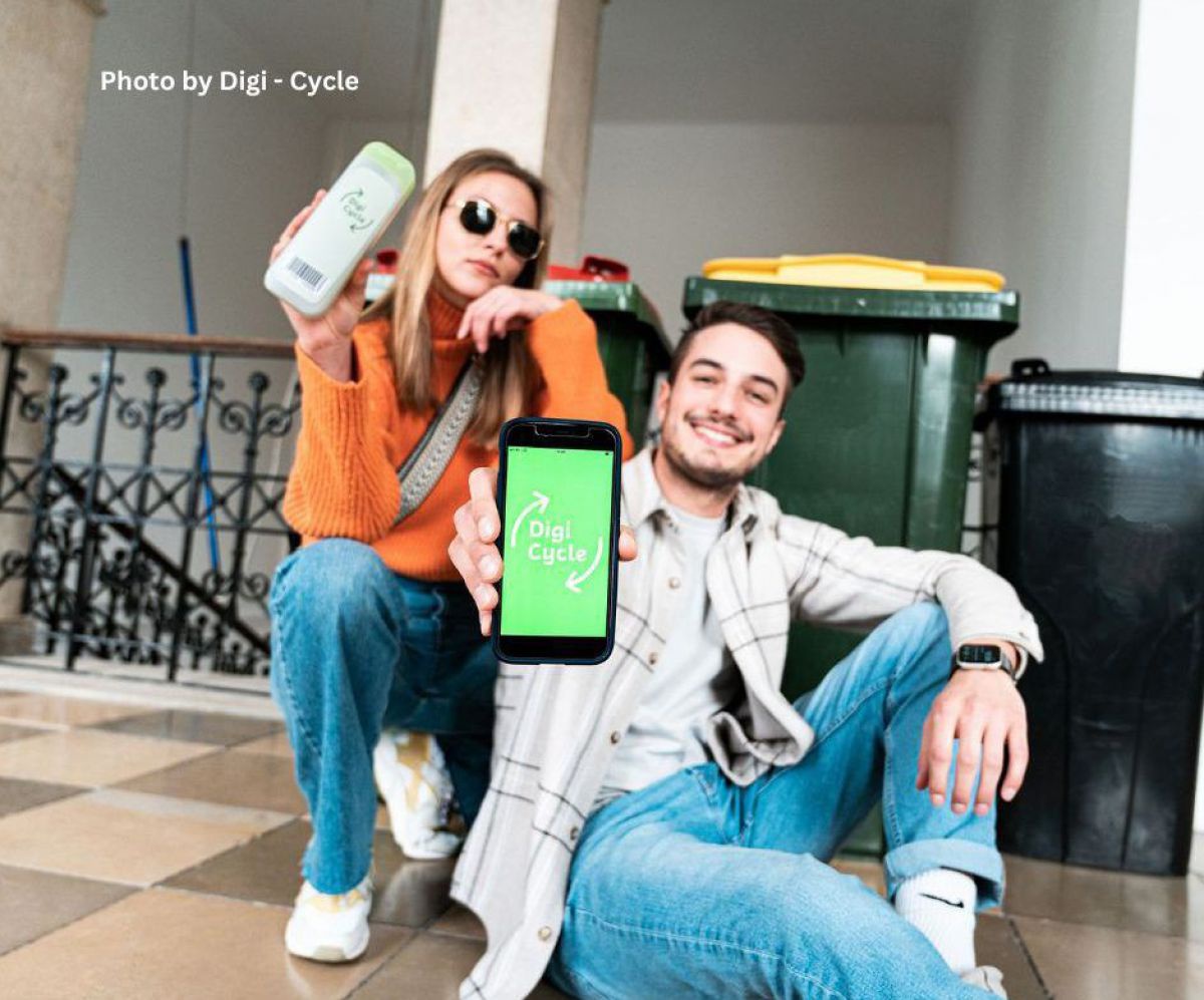 Zwei junge Menschen sitzen vor mehreren Mülltonnen und zeigen die App auf Ihrem Handy.