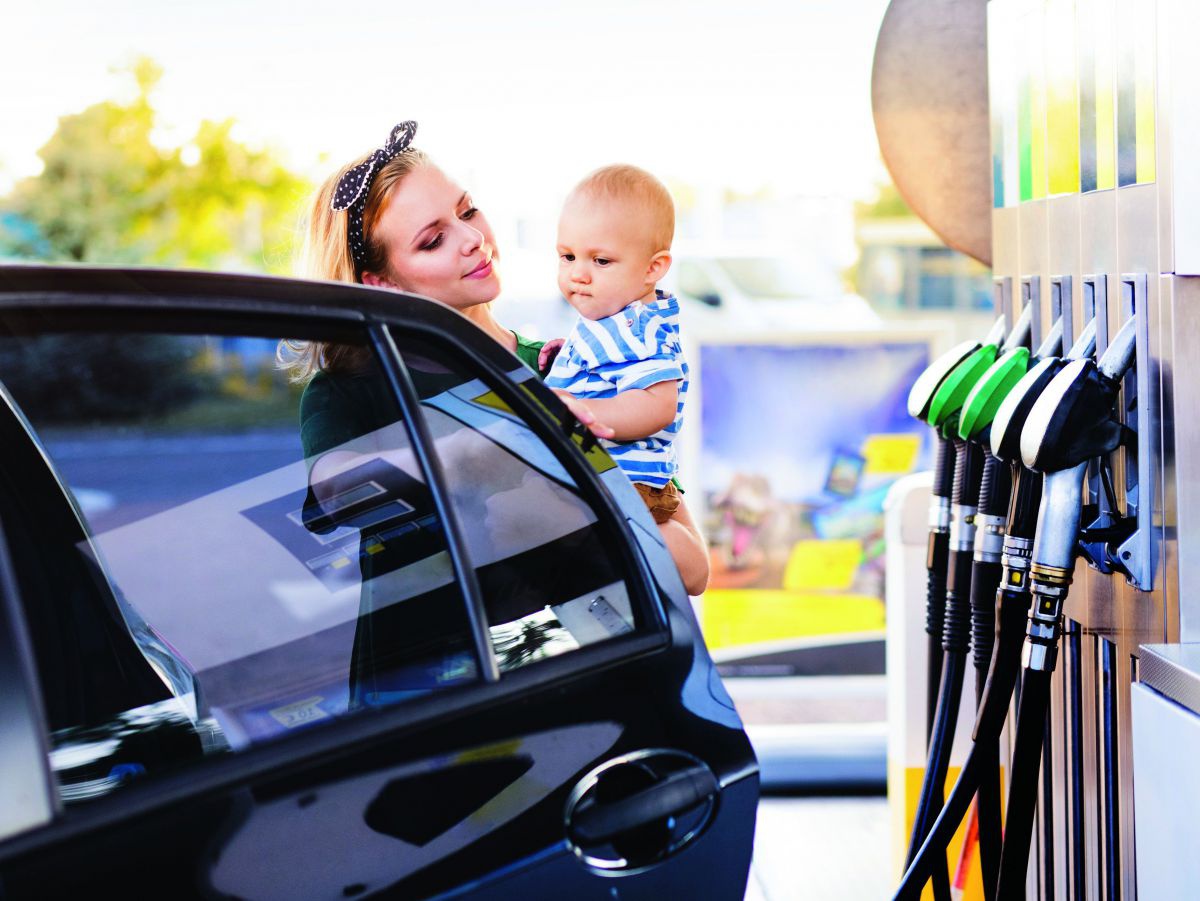 Frau mit Baby auf dem Arm bei Tankstelle.