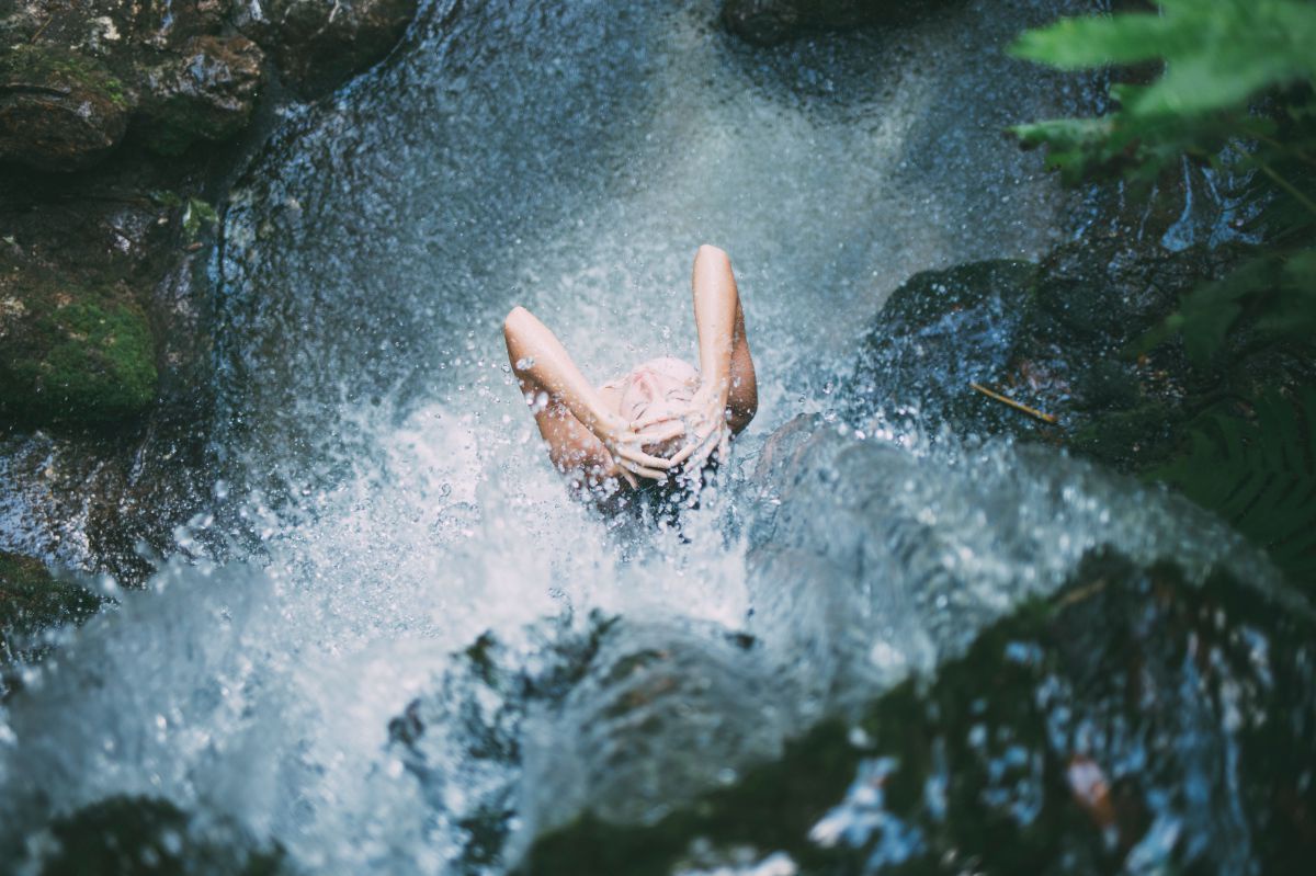 Frau steht unter einem natürlichen Wasserfall wie unter einer Dusche.