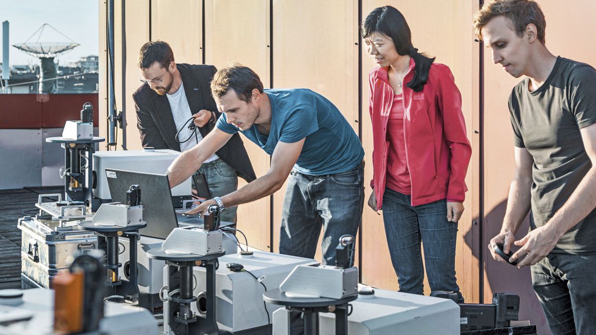 Vier Personen arbeiten an einem kompliziert aussehenden technischen Aufbau.