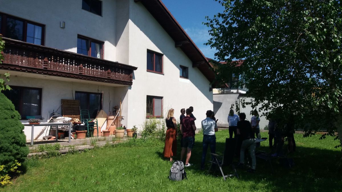 Eine Gruppe von Menschen steht in einem Garten und unterhält sich.