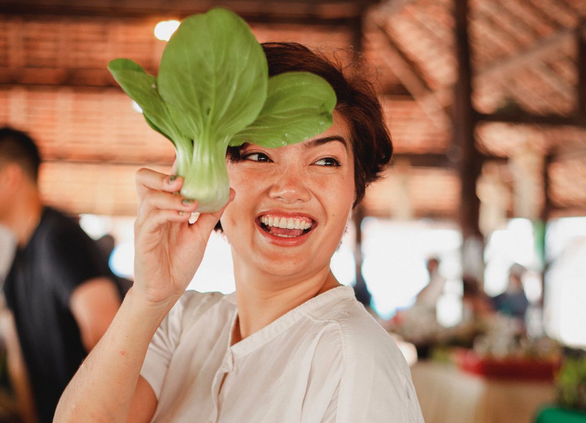 Eine Frau präsentiert lächelnd ein(e) Pak Choi (Gemüse) 