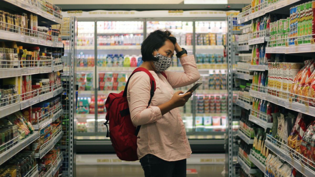 Eine Frau steht vor einem Supermarktregal und greift sich an den Kopf.