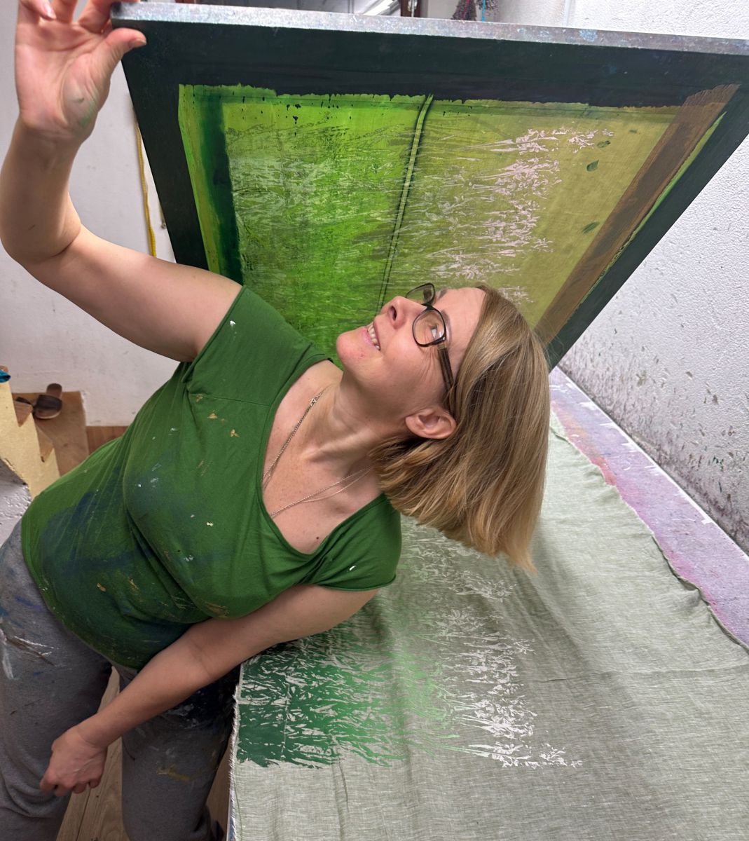 Eine Frau mit blonden Haaren hebt einen Siebdruckrahmen von einem Stoff.