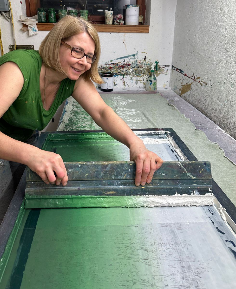 Eine Frau zieht mir einem Spatel Farbe über einen Siebdruck.