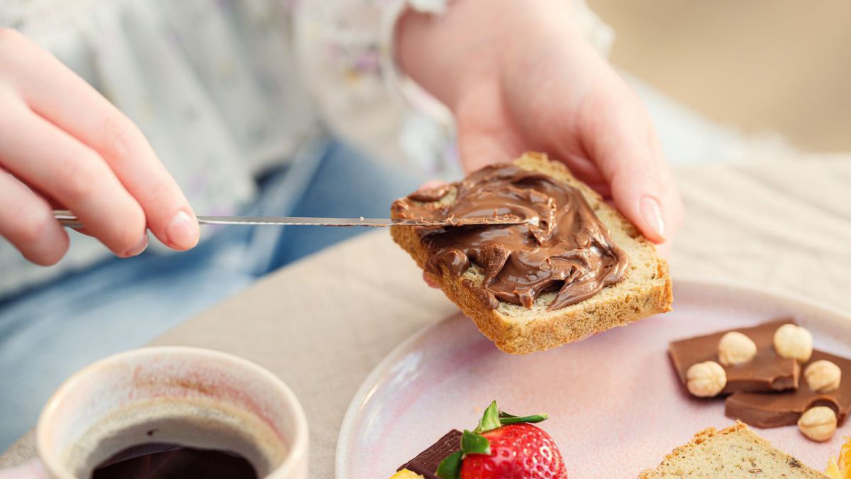 Ein Close-up auf eine Person am Frühstückstisch, die sich einen Nussaufstrich aufs Brot schmiert.