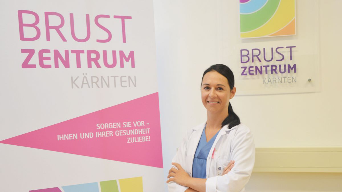 Eine Ärztin mit langen dunklen Haaren steht vor dem Eingangsbereich des Brustkrebszentrums Kärnten.