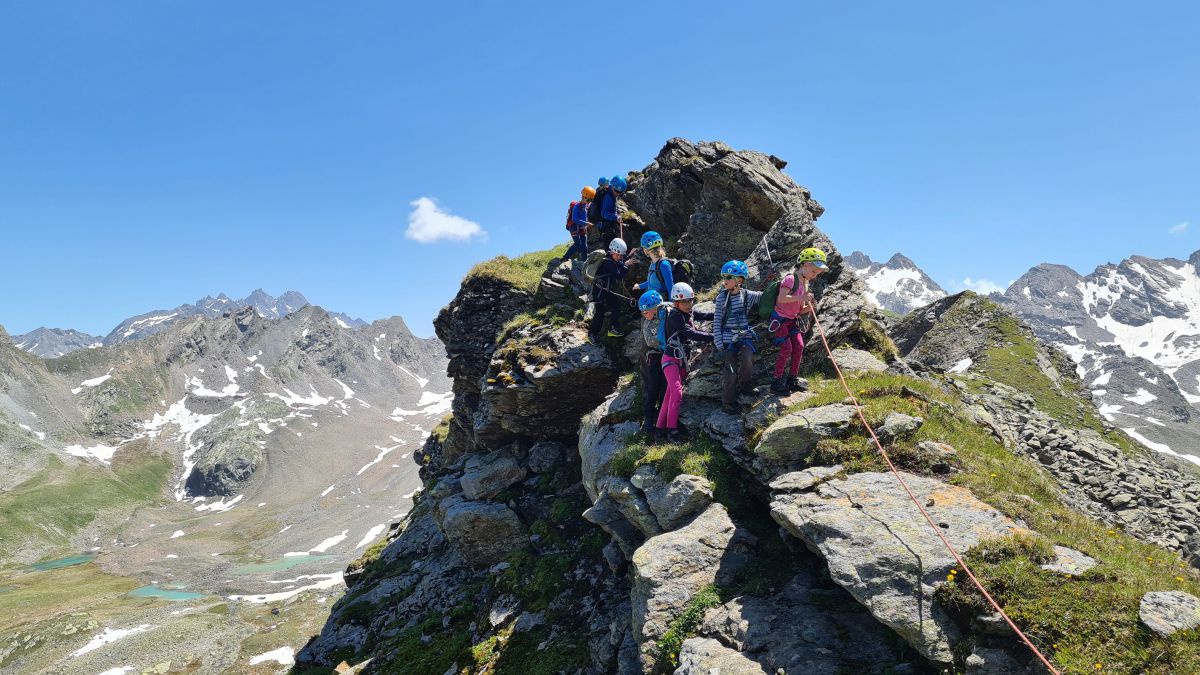 Kinder wanden am Seil gesichert über einen Grat im Gebirge.