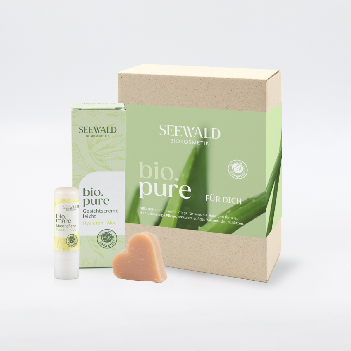 Die bio.pure box ist in Grüntönen gehalten, mit dem Bild von Aloe Vera Blättern. Davor stehen ein Lippenpflegestift sowie eine mittelgroße Schachtel mit der Gesichtsgreme sowie eine Herzseife.