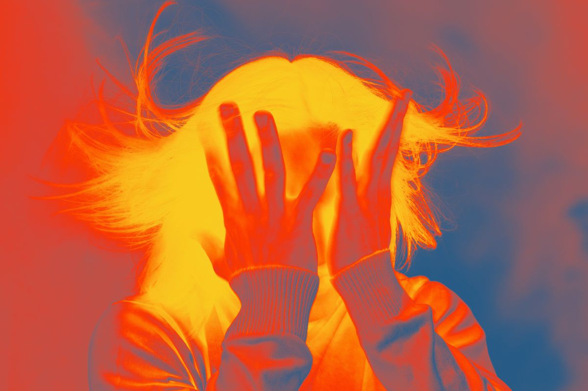 Mit einer Wärmebildkamera aufgenommenes Foto einer Person, die sich sichtlich gestresst beide Hände mit gespreizten Fingern vor das Gesicht hält. Das Farbspektrum bewegt sich von hellem Gelb über Glutrot bis zu kühlem Blau am Rande.