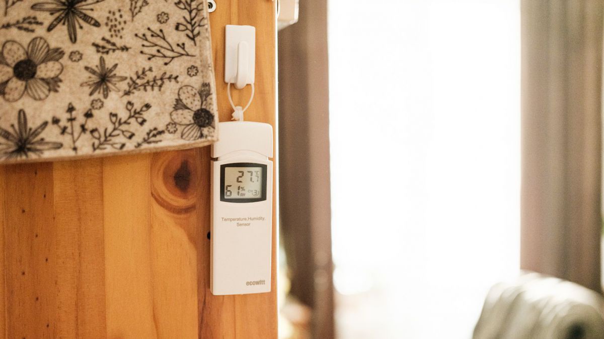 An einem Holzkasten in einem Wohnzimmer hängt ein Temperaturmessgerät