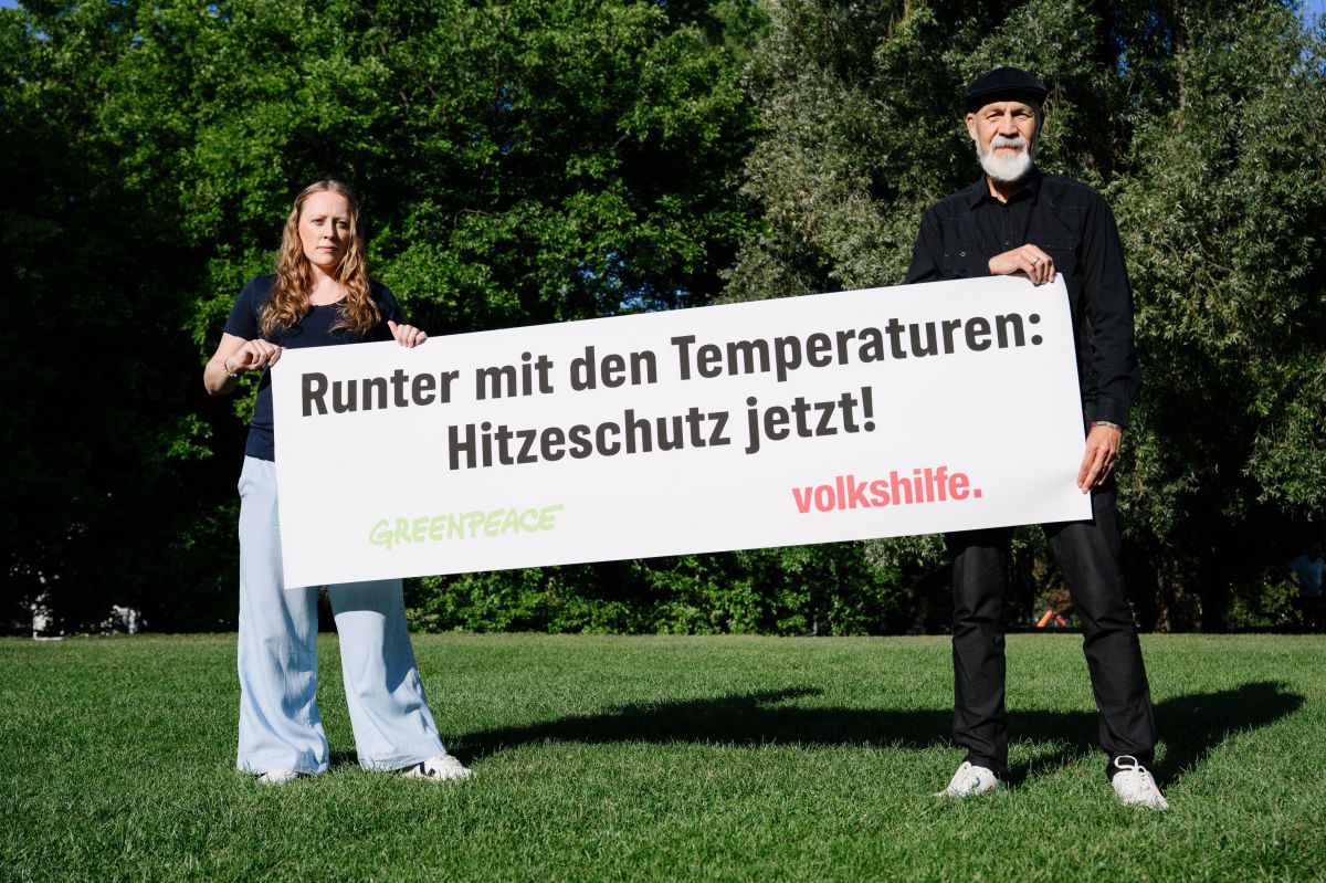Zwei Personen - eine blonde Frau und ein Mann mit weißem Bart - halten ein Banner hoch. Darauf steeht 
