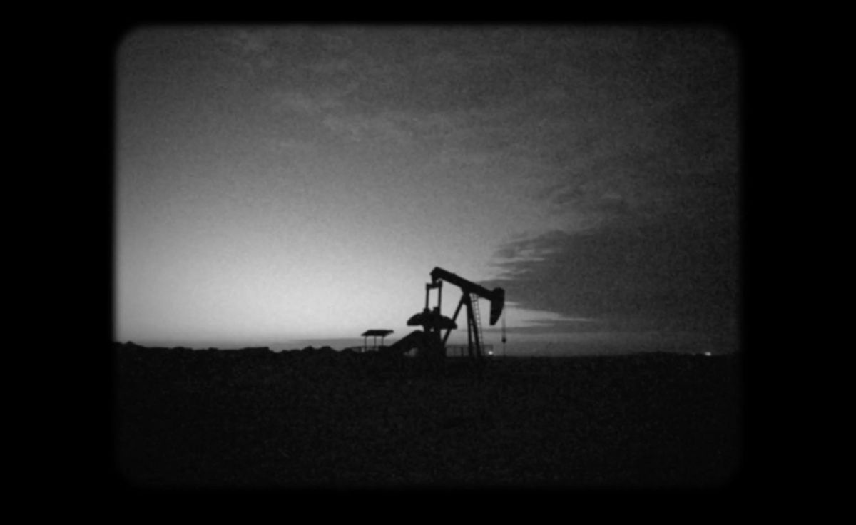 Ein schwarz-weiß Foto einer dunklen Landschaft mit weitem Himmel vor dem sich ein Bohrturm schwarz abhebt.