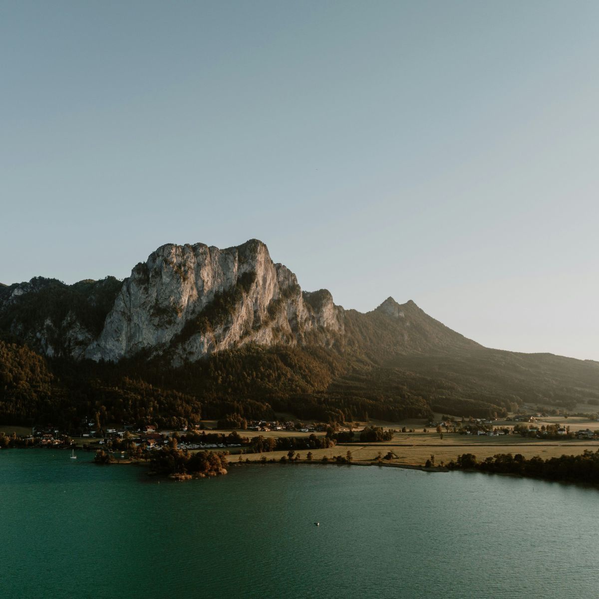 Blick auf die dunkeltürkise Wasserfläche eines Sees, der zwischen Berggipfeln liegt.