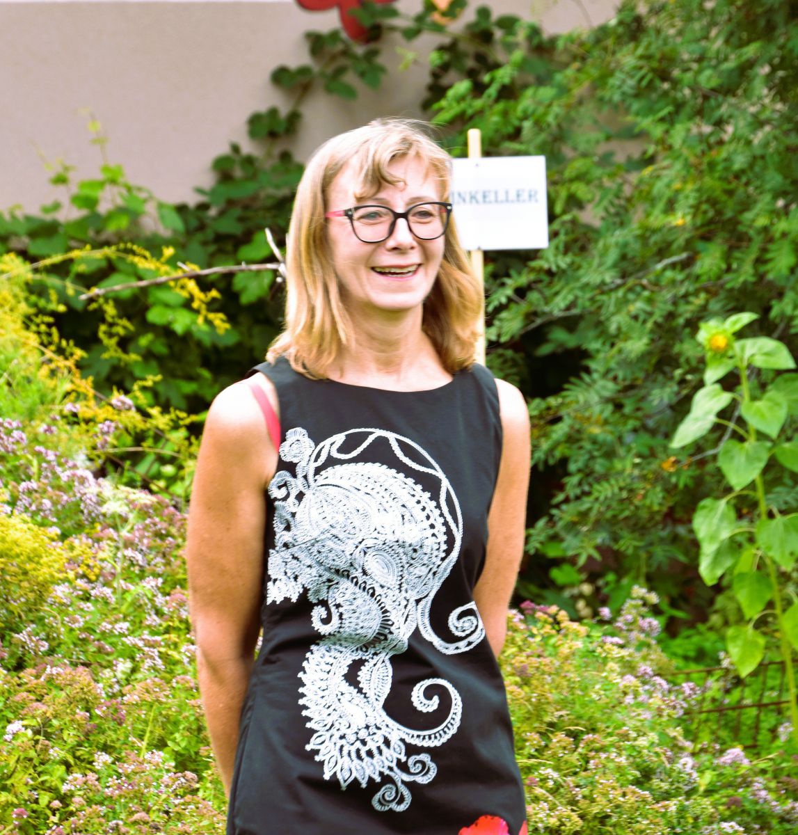 Elisabeth Koppensteiner posiert in einem üppig bewachsenem Garten, hinter ihr ranken sich verschiedene Gewächse um die Wette.