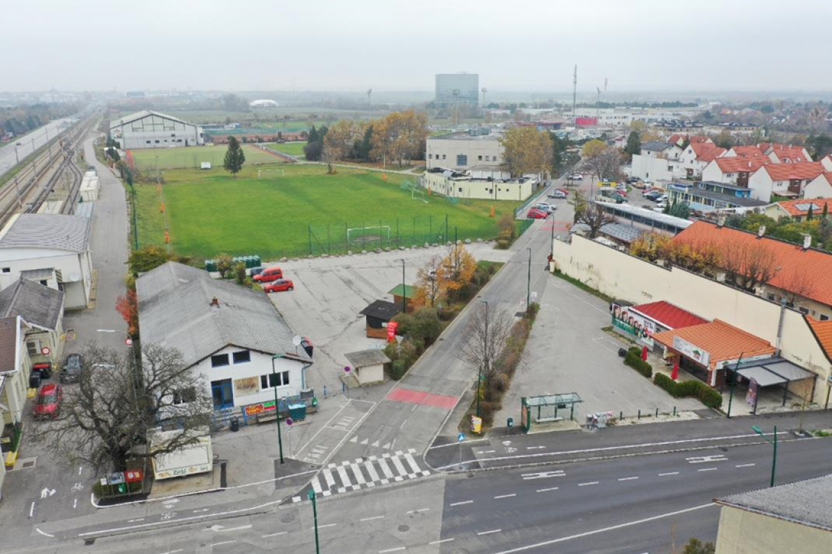 Blick von oben auf einen großteils zubetonierten Platz zwischen Gebäuden und Straßen. 