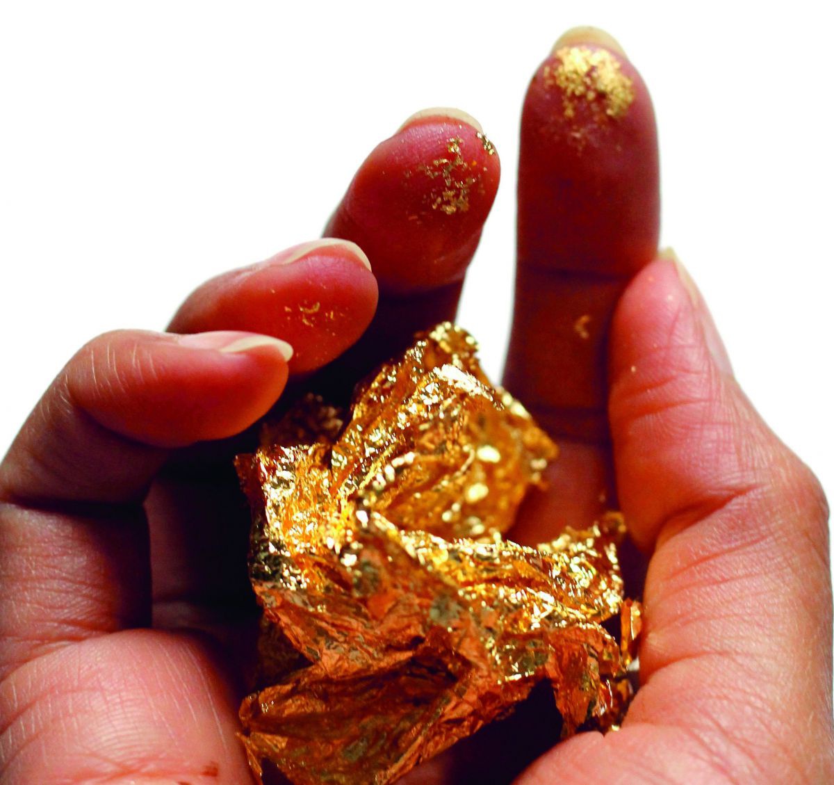 Eine geöffnete Hand hält einen Klumpen Blattgold, auch die Fingerspitzen sind schon etwas vergoldet.