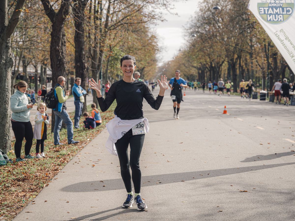 Läufer*innen beim Vienna Climate Run auf einer beidseitig von Bäumen und Zuschauern gesäumten Straße. 