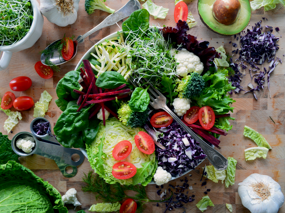 Auf einem Teller ist eine Menge verschiedenstes, großteils fein geschnittenes Gemüse angerichtet: Rotkraut, Salatsorten, rote Rüben, Knoblauch, Avocado, Wirsing, Blattspinat, Kirschtomaten, Broccoli, Kresse, Karfiol, Zucchini... Im Teller liegt oben auf e