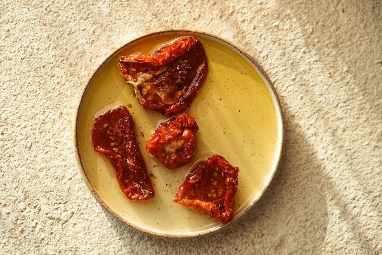 Ein Teller mit vier getrockneten Tomaten und etwas Öl.