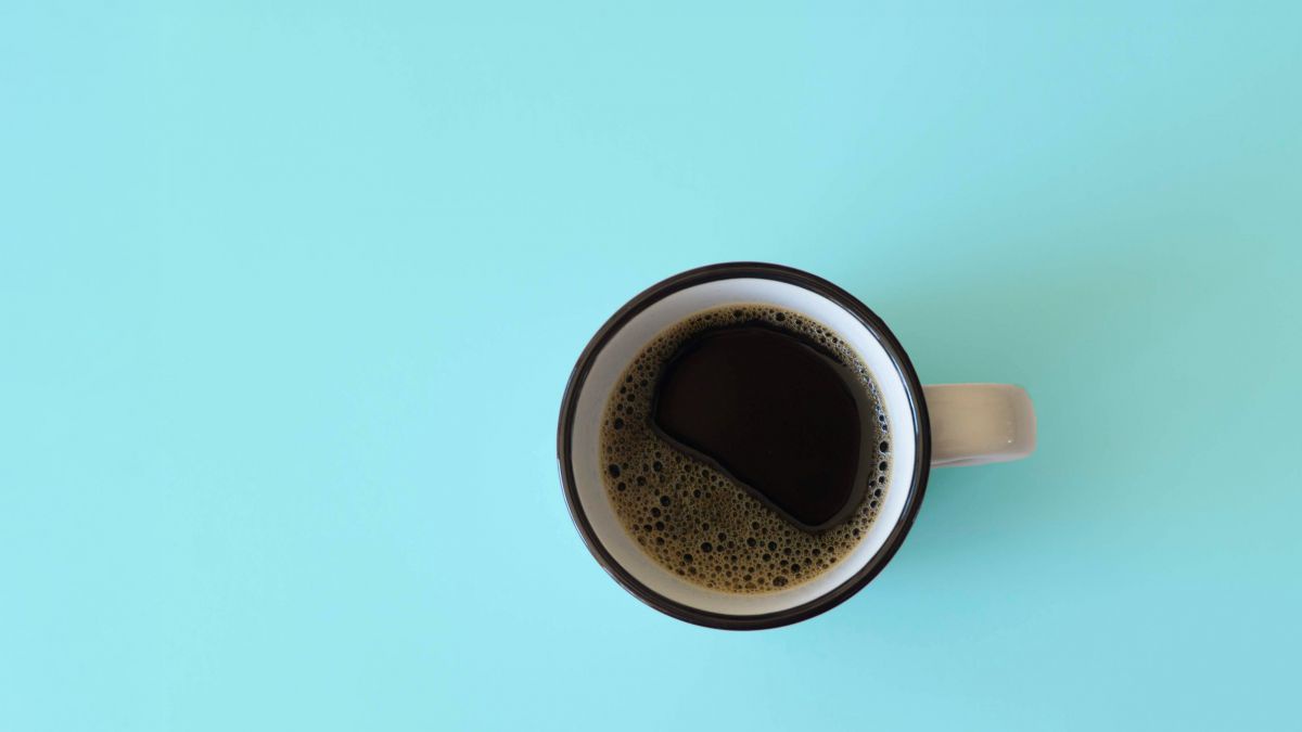 Schwarzer Kaffe in einem Emaille-Häferl mit blauem Rand, von oben fotografiert auf hellblauem Untergrund.
